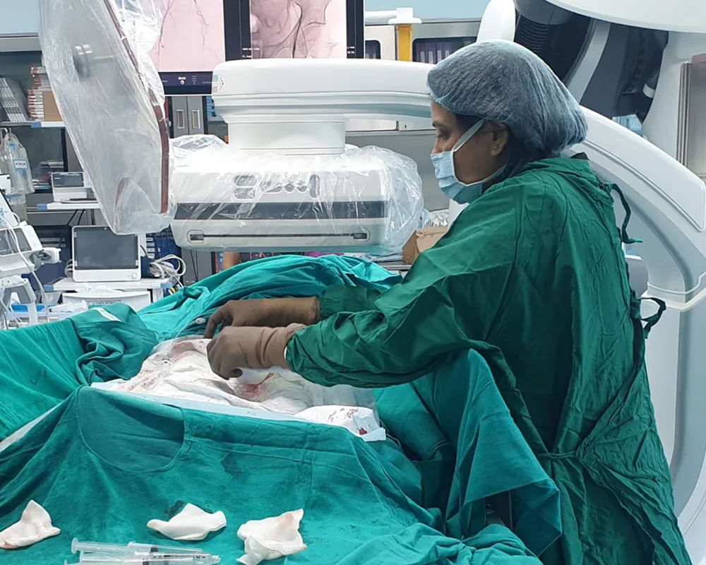 Dr. (Col) Pranati Swain operating in theatre, gowned and masked beside imaging equipment